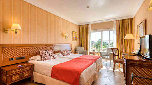 Bilde av et hotellrom med to senger, stol og bord, samt en TV. (AI-generert tekst)