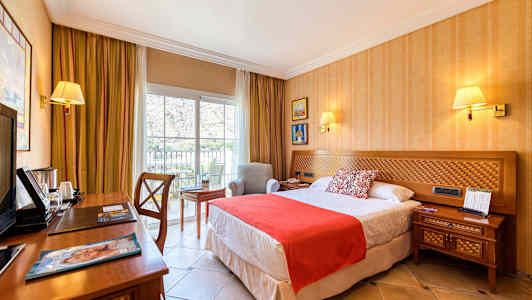 Et hotellrom med en seng, nattbord, skrivebord og en lenestol ved et vindu. (AI-generert tekst)