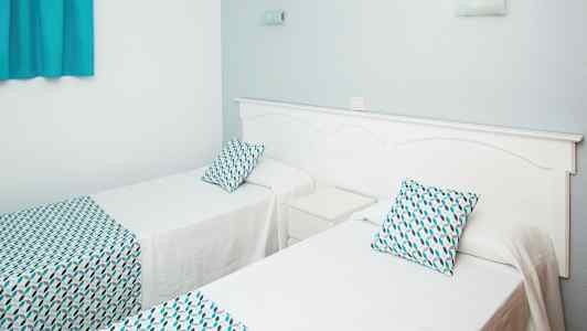 To enkeltsenger med hvite sengeklær og mønstrede puter og sengetepper. (AI-generert tekst)