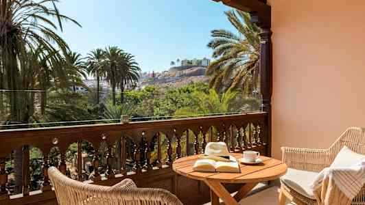 Terrasse med bord, bok og solhatt, utsikt over palmer og bygninger. (AI-generert tekst)