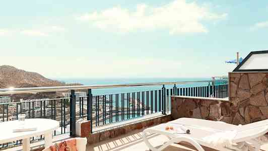 Utsikt fra en terrasse med solsenger og hav i bakgrunnen. (AI-generert tekst)