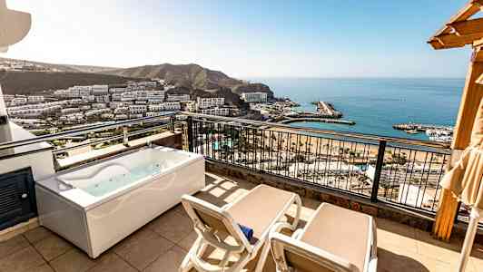 Balkong med to solsenger og et boblebad, utsikt over havet og omgivelsene. (AI-generert tekst)