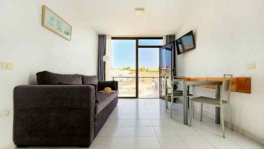 En stue med en mørk sofa, et spisebord med stoler og en balkong med utsikt. (AI-generert tekst)