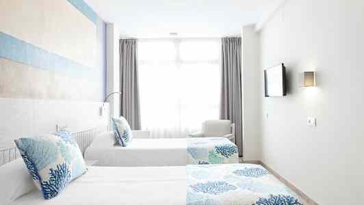 To enkeltsenger med blått og hvitt sengetøy i et lyst rom med et stort vindu. (AI-generert tekst)