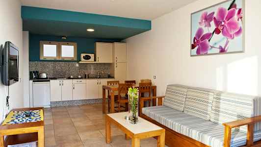 En åpen planløsning med kjøkken og stue, møblert med trebord og sofa. (AI-generert tekst)