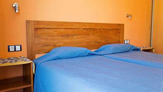 En seng med blåprikkete sengetøy og en tre hodegjerde mot en oransje vegg. (AI-generert tekst)