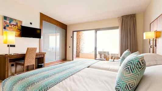 Bilde av et hotellrom med to senger, en skrivebordsplass, en TV og en balkong med stoler. (AI-generert tekst)