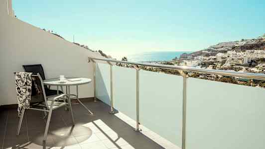 Balkong med bord og stol, utsikt mot havet og bebyggelse. (AI-generert tekst)