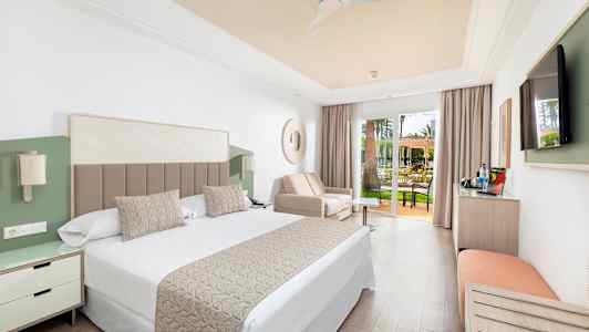 Et hotellrom med dobbeltseng, sofa og glassdører til en terrasse. (AI-generert tekst)