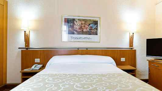 Hotellseng med hvite laken, en beige dekorasjon, to sengelamper og et veggbilde i bakgrunnen. (AI-generert tekst)