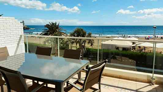 En møbelgruppe på en balkong med utsikt over stranden og havet. (AI-generert tekst)