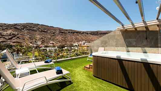 Bilde av en terrasse med gresslagt område, solsenger og en jacuzzi med utsikt over et fjellandskap. (AI-generert tekst)