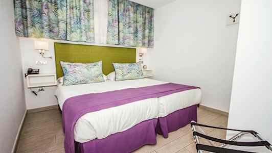 Soverom med en dobbeltseng, grønn sengegavl, lilla sengeteppe og gardiner med mønster. (AI-generert tekst)