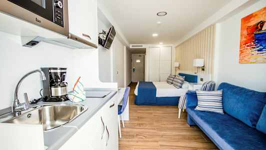 Et hotellrom med en seng, blå sofa og kjøkkenkrok med vask. (AI-generert tekst)