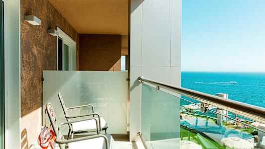 Balkong med to stoler, glassrekkverk og utsikt over havet. (AI-generert tekst)