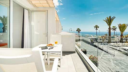 En solrik terrasse med utsikt over havet, utstyrt med en hvit sittegruppe. (AI-generert tekst)