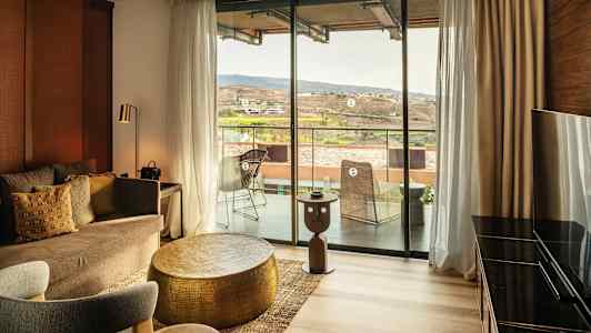 En innredet hotellsuite med en sittegruppe og utsikt mot en balkong og landskap. (AI-generert tekst)