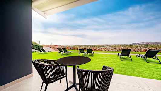 En uteplass med bord, stoler, gressplen og solsenger, med utsikt over landskapet. (AI-generert tekst)