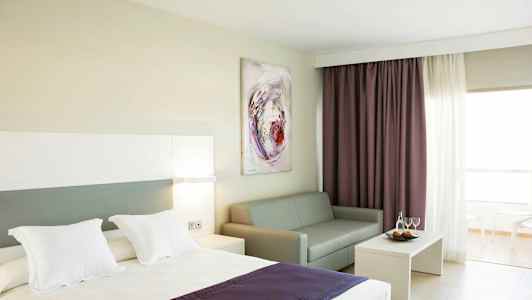 Hotellrom med seng, sofa, sofabord og gardiner. (AI-generert tekst)