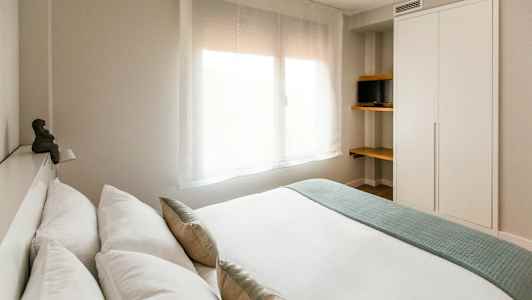 Moderne soverom med et stort vindu, et skap og hyller med en liten TV. (AI-generert tekst)