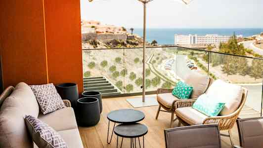 Terrasse med sittemøbler under en parasoll og utsikt over havet. (AI-generert tekst)