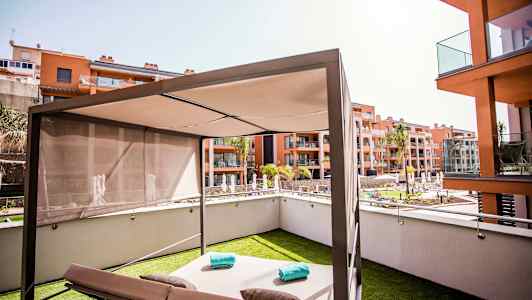 En moderne solseng med parasoll på en gressplen, omgitt av boligbygg og et svømmebasseng. (AI-generert tekst)