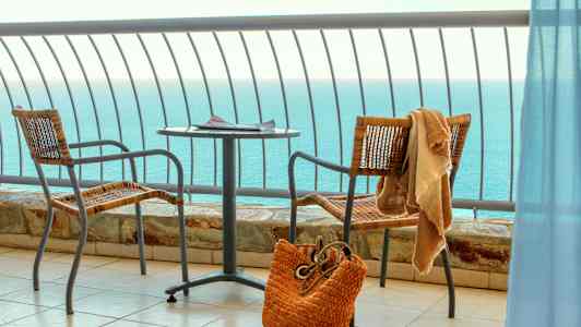 Utsikt over havet fra en balkong med bord, to stoler og en strandveske. (AI-generert tekst)