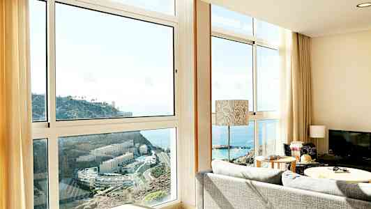 Stue med store vinduer som viser utsikt over havet og en klippe. (AI-generert tekst)