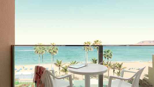 Balkong med utsikt over strand og hav, bord og stoler synlige. (AI-generert tekst)