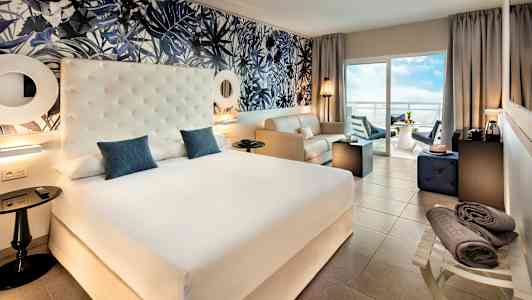 Hotellrom med stor seng, sittegruppe og balkong med utsikt. (AI-generert tekst)