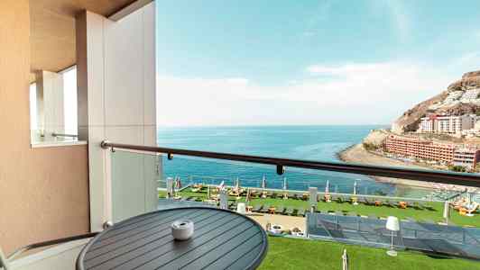 Utsikt fra en balkong mot havet og en frodig hotellhage. (AI-generert tekst)