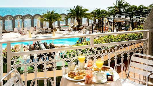 Utsikt fra en balkong med frokostservise mot bassengområde og havet. (AI-generert tekst)