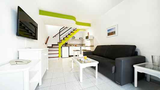 Et hotellrom med sofa, sofabord, TV og liten kjøkkenkrok. (AI-generert tekst)