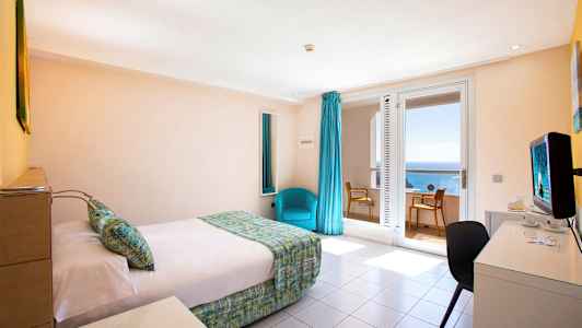 Et hotellrom med en seng, et skrivebord og en stol. Vinduer med havutsikt. (AI-generert tekst)