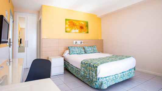 Et hotellrom med en dobbeltseng, veggmaleri av blomster over sengen og lyse vegger. (AI-generert tekst)