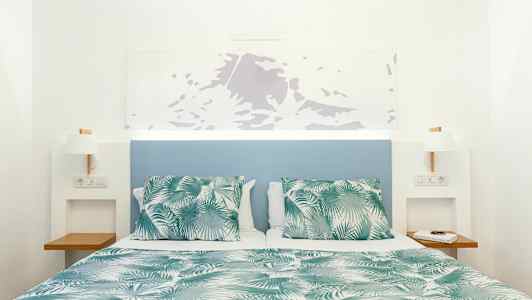 Seng med grønn- og hvitmønstret dyne og puter, med blå sengegavl og hvite vegger. (AI-generert tekst)