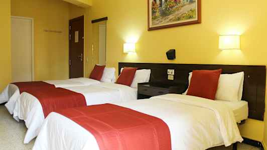 Hotellrom med to enkeltsenger, hvite laken og røde dekorative sengetepper. (AI-generert tekst)