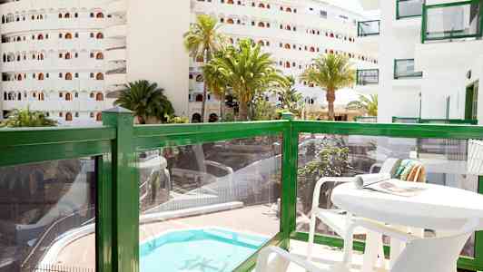 Balkong med bord og stoler, utsikt over et basseng og omkringliggende bygninger. (AI-generert tekst)