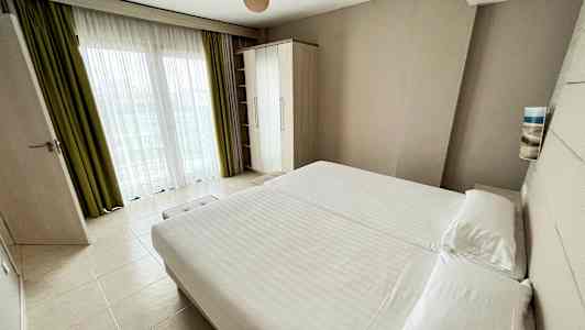 Et hotellrom med stor seng, garderob og vindu med gardiner. (AI-generert tekst)