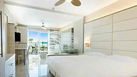 Lyst hotellrom med stor seng, glassvegg og adgang til balkong. (AI-generert tekst)