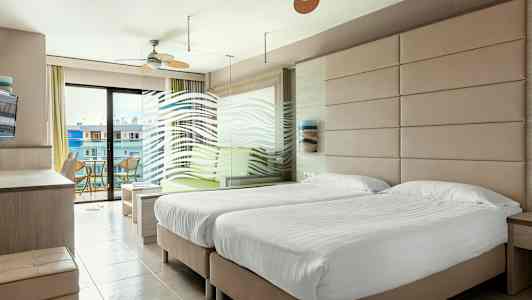 Et hotellrom med to enkeltsenger, en sittegruppe og en balkong med utsikt. (AI-generert tekst)