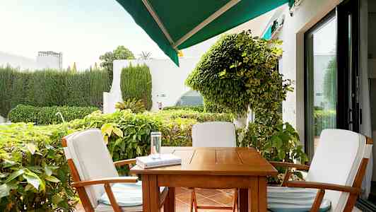 Utemøbler med tre stoler rundt et bord på en terrasse, omgitt av beplantning. (AI-generert tekst)