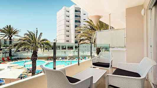 Utsikt fra en terrasse med sittegruppe, basseng og omkringliggende bygninger. (AI-generert tekst)