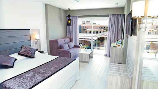 Hotellrom med seng, sofa og balkongutsikt. (AI-generert tekst)