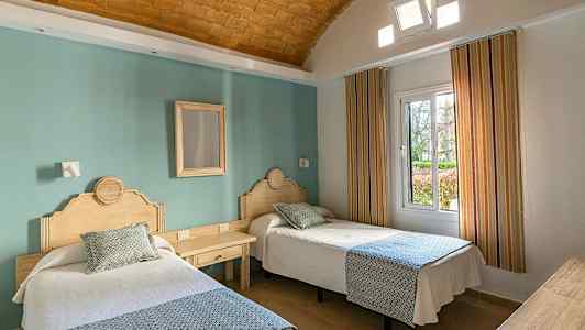 To enkeltsenger med trehodet gavler i et hotellrom med en grønn vegg og vindu. (AI-generert tekst)