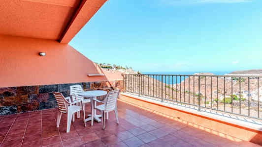 Terrasse med bord, stoler og rekkverk, samt havutsikt. (AI-generert tekst)