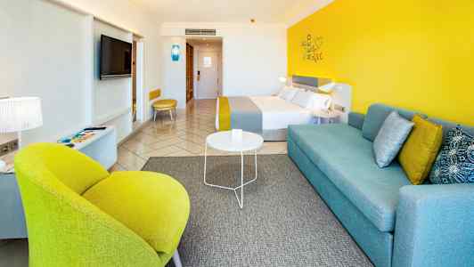 Moderne innredet hotellrom med fargerike detaljer som gul stol og blå sofa. (AI-generert tekst)