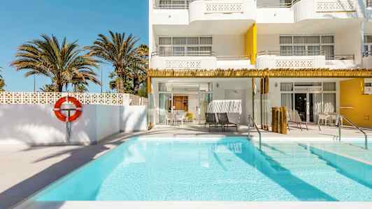 Utendørsbasseng ved et hotell med hvite og gule fasader, omgitt av palmer. (AI-generert tekst)