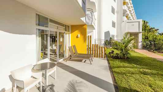 En solrik terrasse med to stoler og et bord ved siden av glassdører. (AI-generert tekst)