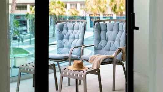 To blå stoler og en krakk med en hatt på en balkong. (AI-generert tekst)